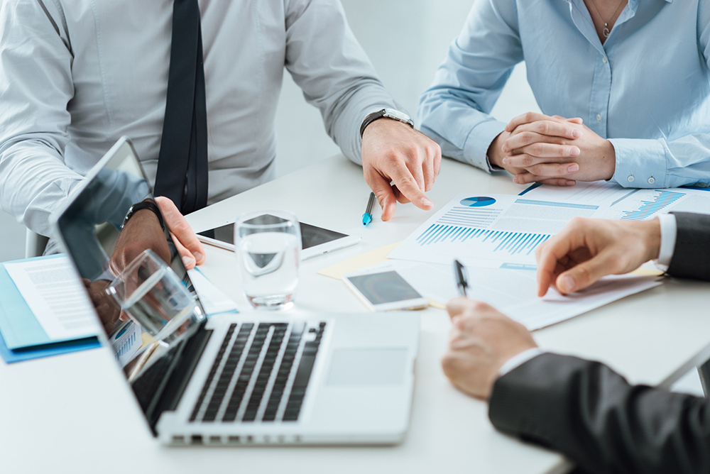 team of three people working at a table with a laptop, mobile devices, and business papers