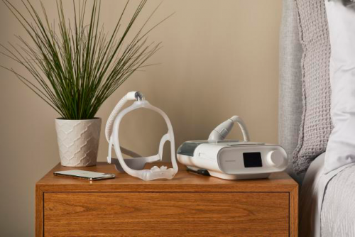 CPAP and mask sitting on nightstand next to a decorative plant