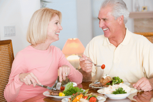 Man and woman sitting at table smiling and eating a healthy meal