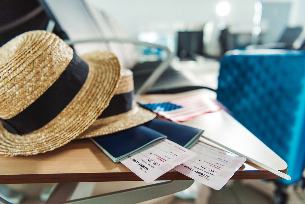 straw hats and plane tickets on a table with a suitcase nearby