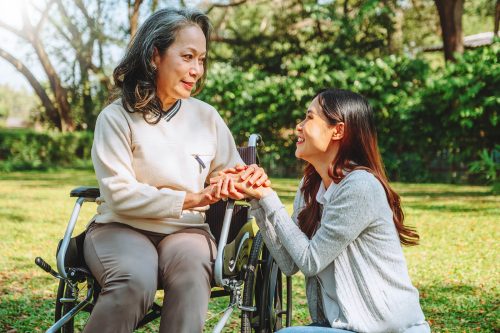 Grandmother in wheelchair with caretaker kneeling next to her in a sunny park