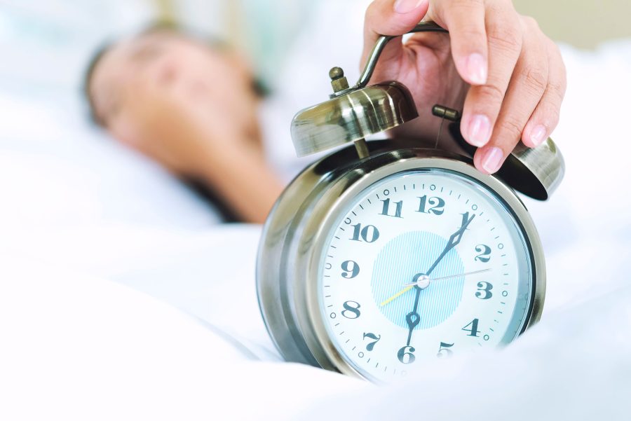 person in bed reaching out to silence alarm clock