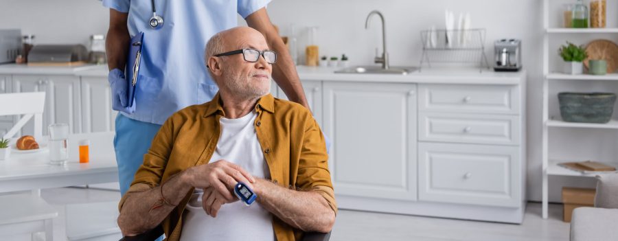 Elderly man wearing a pulse oximeter at home with a nurse