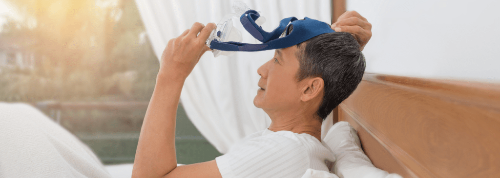 Man sitting in bed in the morning, pulling his CPAP mask off his face