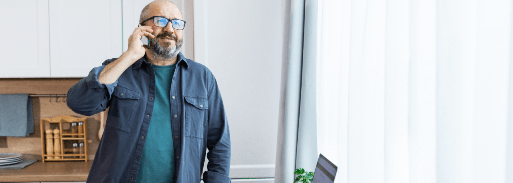 Man standing in his kitchen on the phone and smiling