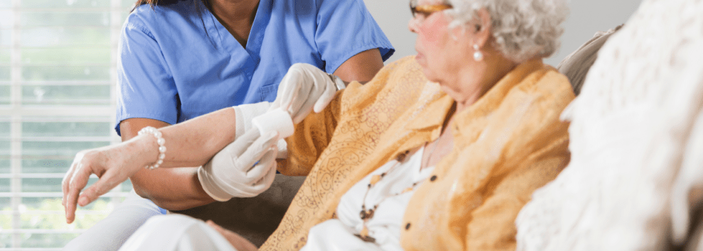 Image shows nurse bandaging senior woman's arm at home