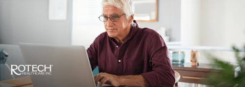 Older man with glasses sitting at the table using his laptop