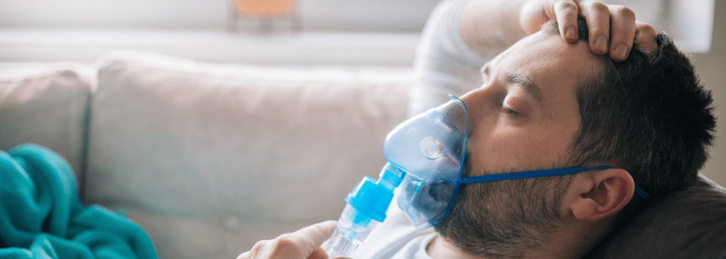 Man lying on couch with hand on his head, holding oxygen mask to his mouth