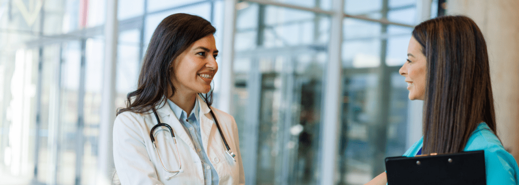 Two healthcare professionals speaking outside and smiling