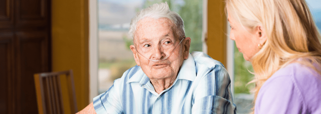 Senior man with oxygen on sitting at table speaking with a woman