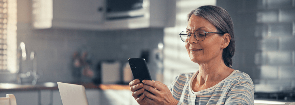 Senior woman looking at phone for answers to common questions while sitting in her kitchen
