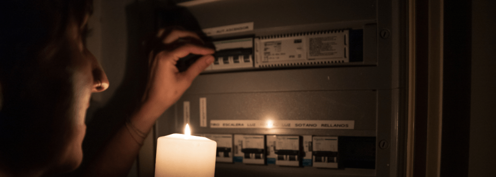 Unrecognizable woman with a lighted candle checking if there is light in the electrical panel