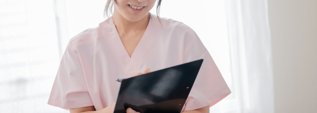 Healthcare professional in scrubs writing on clipboard and smiling
