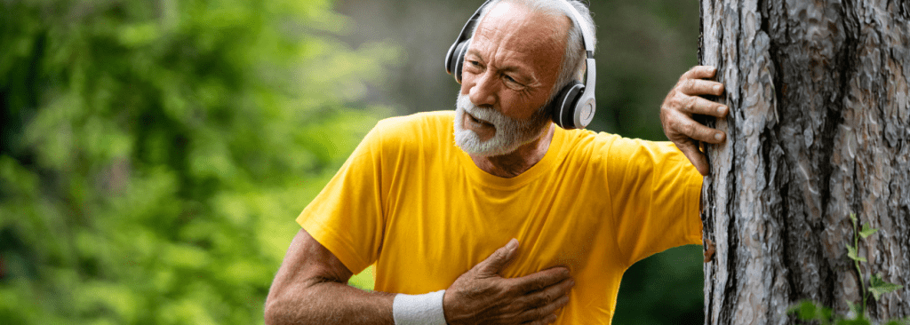 Active senior man leaning against a tree trying to breathe while walking outdoors