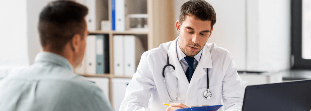Male doctor speaking to male patient while reviewing clipboard