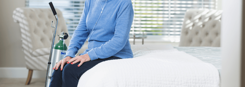 Woman sitting at home on bed with oxygen tank near her