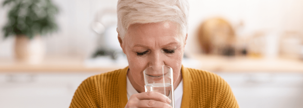 Senior woman drinking water at table in her kitchen