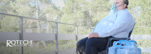 Man sitting on bench outside using oxygen concentrator with mask on