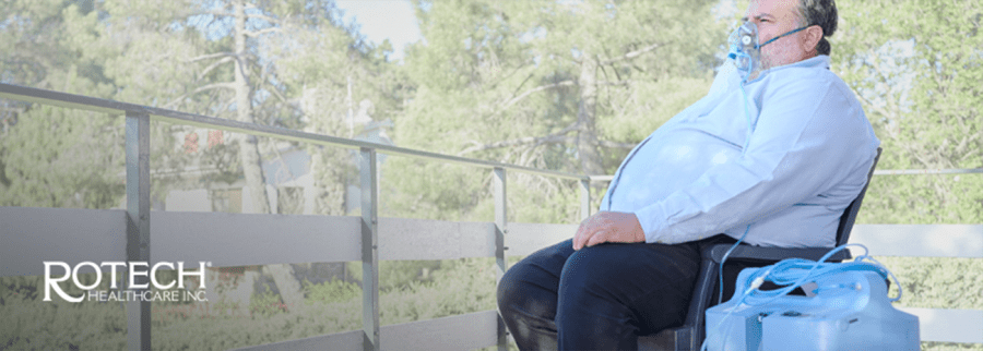 Man sitting on bench outside using oxygen concentrator with mask on