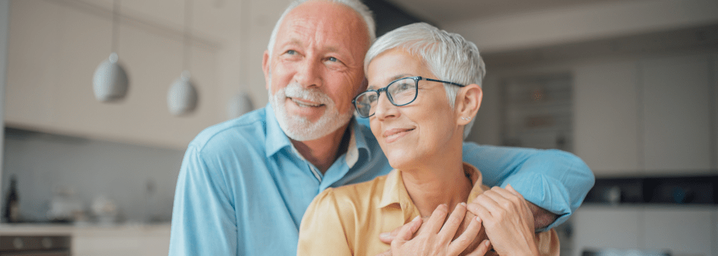 Senior man smiling with his arm around his smiling wife in their kitchen
