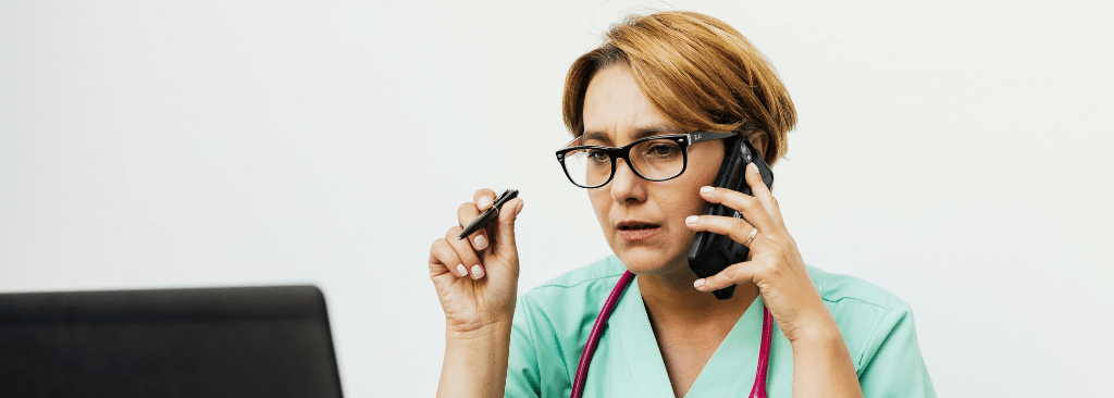 Female healthcare professional speaking on the phone and holding pen out