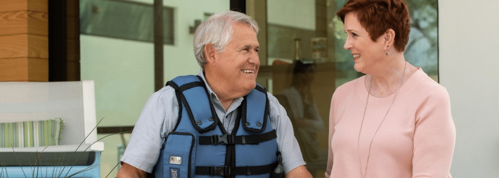 Senior man wearing AffloVest smiling at wife as they sit on steps outside home