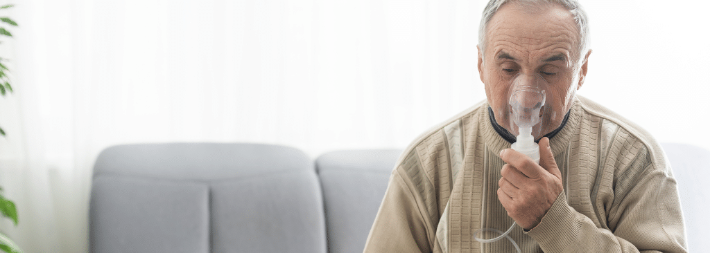 Senior man with COPD using oxygen mask while sitting on couch at home