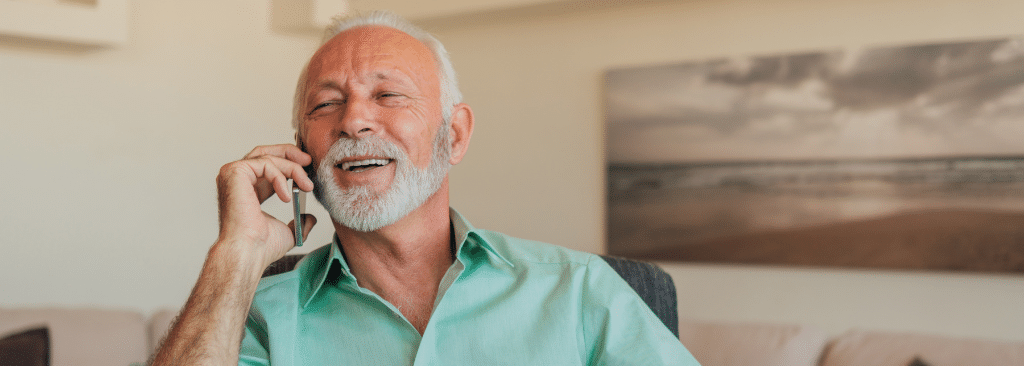 Senior man sitting in chair at home smiling while on the phone