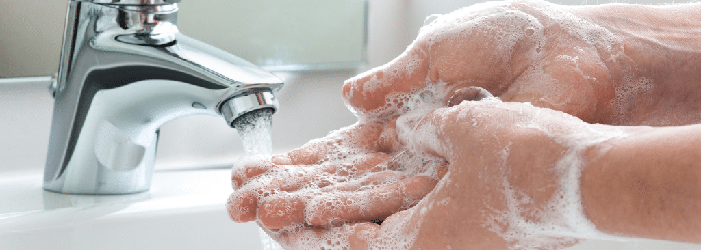 Person rubbing soap on their hands in front of running faucet at the sink